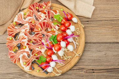 Şişe üzerinde piknik atıştırmalıkları. Jamon, mozzarella, kiraz domatesleri, bezelyeler, taze yeşiller. Modern duruş, ahşap arkaplan, üst manzara