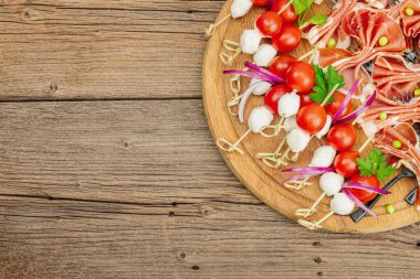 Şişe üzerinde piknik atıştırmalıkları. Jamon, mozzarella, kiraz domatesleri, bezelyeler, taze yeşiller. Modern duruş, ahşap arkaplan, üst manzara