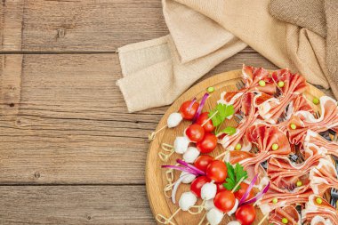 Şişe üzerinde piknik atıştırmalıkları. Jamon, mozzarella, kiraz domatesleri, bezelyeler, taze yeşiller. Modern duruş, ahşap arkaplan, üst manzara