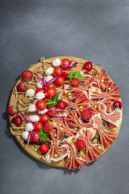 Şişe üzerinde piknik atıştırmalıkları. Jamon, mozzarella, kiraz domatesleri, bezelyeler, taze yeşiller. Sert ışık, karanlık gölge, siyah taş arka plan, üst görüş