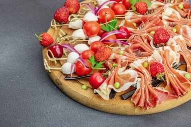 Şişe üzerinde piknik atıştırmalıkları. Jamon, mozzarella, kiraz domatesleri, bezelyeler, taze yeşiller. Siyah taş beton arka plan, kapat