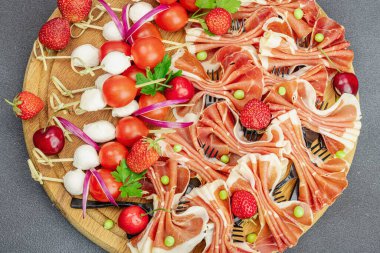 Şişe üzerinde piknik atıştırmalıkları. Jamon, mozzarella, kiraz domatesleri, bezelyeler, taze yeşiller. Siyah taş beton arka plan, kapat