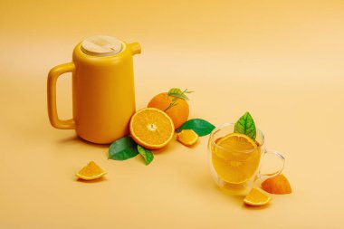 Seramik çay demliğinde portakal çayı ve olgun meyveler. Serinletici mevsimlik içecek, yeşil narenciye yapraklı kavramsal arka plan. Modern biçim, seçici odak, kopyalama alanı