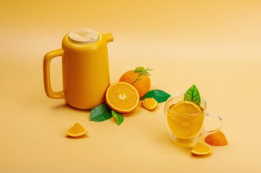 Seramik çay demliğinde portakal çayı ve olgun meyveler. Serinletici mevsimlik içecek, yeşil narenciye yapraklı kavramsal arka plan. Modern biçim, seçici odak, kopyalama alanı