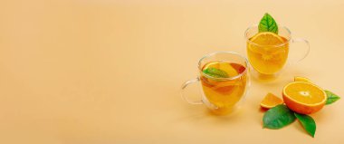 Cam bardakta portakal çayı ve olgun meyveler. Serinletici mevsimlik içecek, yeşil narenciye yapraklı kavramsal arka plan. Modern biçim, seçici odak, pankart biçimi