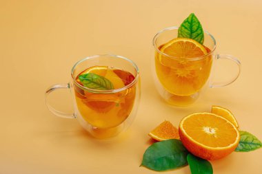 Cam bardakta portakal çayı ve olgun meyveler. Serinletici mevsimlik içecek, yeşil narenciye yapraklı kavramsal arka plan. Modern biçim, seçici odak, kopyalama alanı