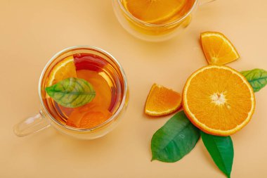 Cam bardakta portakal çayı ve olgun meyveler. Serinletici mevsimlik içecek, yeşil narenciye yapraklı kavramsal arka plan. Modern tarz, seçici odak, üst görünüm