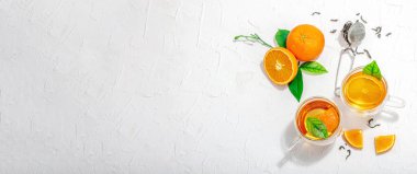 Cam bardakta portakal çayı ve olgun meyveler. Serinletici mevsimlik içecek, yeşil narenciye yapraklı kavramsal arka plan. Modern tarz, seçici odak, sert ışık, karanlık gölge, afiş biçimi