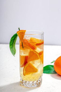 Buzlu ve olgun meyveli portakal kokteyli. Serinletici mevsimlik içecek, yeşil narenciye yapraklı kavramsal arka plan. Modern biçim, seçici odak, sert ışık, karanlık gölge, kopyalama alanı