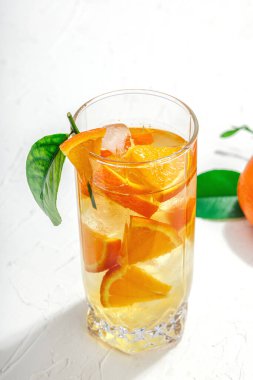 Buzlu ve olgun meyveli portakal kokteyli. Serinletici mevsimlik içecek, yeşil narenciye yapraklı kavramsal arka plan. Modern biçim, seçici odak, sert ışık, karanlık gölge, kopyalama alanı