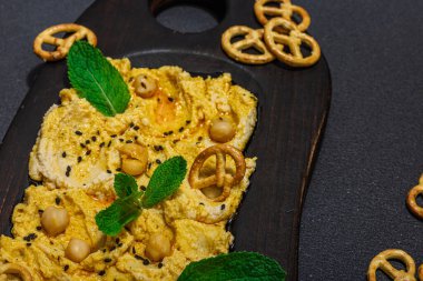 Humus, simit ve taze nane yapraklı tereyağlı gıda trendi. Parti için aperatif, vejetaryen aperatifi, sert ışık, karanlık gölge. Siyah taş zemin, düz zemin, üst manzara