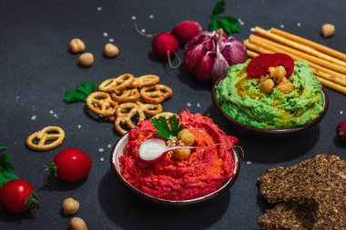 Çeşitli humus sosları, taze sebzeler ve otlar. Çıtır ekmekler, modern vegan sağlıklı yiyecekler. Sert ışık, karanlık gölge, siyah taş beton arka plan, kapat