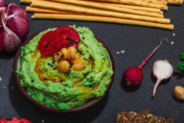 Çeşitli humus sosları, taze sebzeler ve otlar. Çıtır ekmekler, modern vegan sağlıklı yiyecekler. Sert ışık, karanlık gölge, siyah taş beton arka plan, kapat