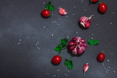 Taze sebzeler ve otlarla mutfak arka planı. Domates, kiraz, sarımsak, deniz tuzu ve maydanoz. Düz yatıyordu, sert ışık, karanlık gölge, siyah taş beton zemin