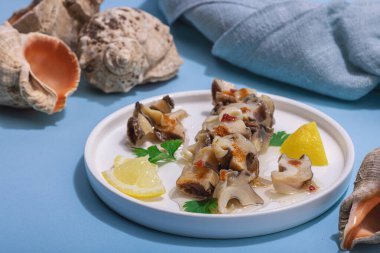 Yağlı, baharatlı ve yeşillikli turşulu rapan eti. Omega zengini sağlıklı deniz ürünleri. Deniz dekoratif aksesuarı, sert ışık, koyu gölge, mavi arkaplan, kapat