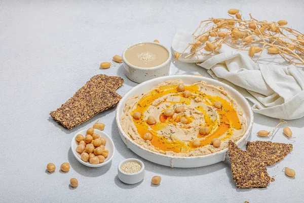 Stock image Hummus with olive oil and crispy bread. Indispensable ingredient for healthy lifestyle. Comfort food, vegan snack. Hard light, dark shadow, stone concrete background, flat lay, copy space