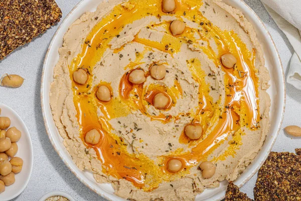 stock image Hummus with olive oil and crispy bread. Indispensable ingredient for healthy lifestyle. Comfort food, vegan snack. Hard light, dark shadow, stone concrete background, flat lay, top view