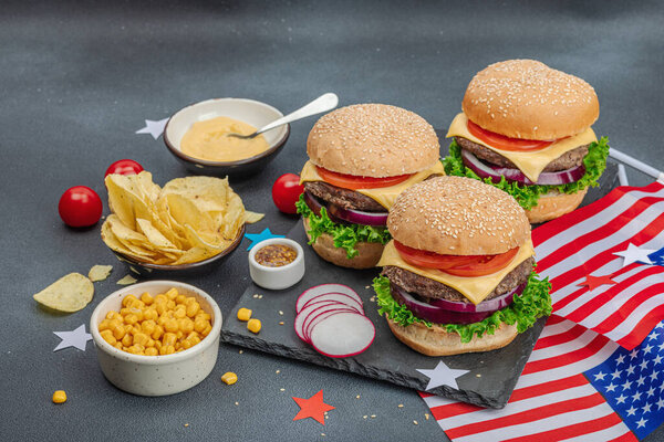 Homemade burgers. An American classic, traditional food for picnic, party or celebration Independence Day. Sauce, chips, sweet corn. Dark stone concrete background, close up