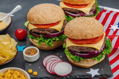 Ev yapımı hamburgerler. Amerikan klasiği, geleneksel piknik, parti ya da Bağımsızlık Günü yemeği. Sos, cips, tatlı mısır. Koyu taş beton arka plan, kapat