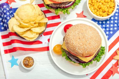 Ev yapımı hamburgerler. Amerikan klasiği, geleneksel piknik, parti ya da Bağımsızlık Günü yemeği. Sert ışık, karanlık gölge, düz yer, beyaz ahşap zemin, üst manzara