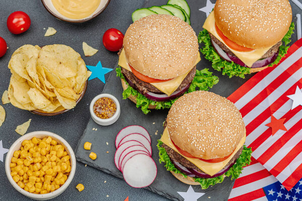 Homemade burgers. An American classic, traditional food for picnic, party or celebration Independence Day. Sauce, chips, sweet corn. Dark stone concrete background, top view