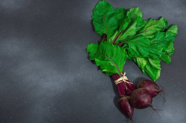 Taze pancar kökü, yemek pişirmek için sağlıklı malzeme. Modaya uygun sert ışık, koyu gölge, siyah taş arka plan, düz yer, üst manzara