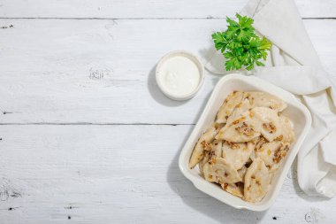 Lahanayla dolu börekler. Kızarmış soğan, taze ekşi krema. Geleneksel Ukrayna yemeği, moda vejetaryen yemekleri. Sert ışık, karanlık gölge, beyaz ahşap zemin, üst manzara