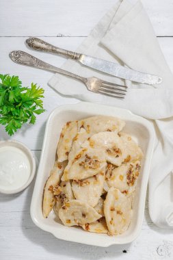 Lahanayla dolu börekler. Kızarmış soğan, taze ekşi krema. Geleneksel Ukrayna yemeği, moda vejetaryen yemekleri. Sert ışık, karanlık gölge, beyaz ahşap zemin, üst manzara