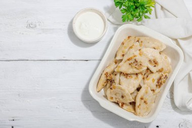 Lahanayla dolu börekler. Kızarmış soğan, taze ekşi krema. Geleneksel Ukrayna yemeği, moda vejetaryen yemekleri. Sert ışık, karanlık gölge, beyaz ahşap zemin, üst manzara