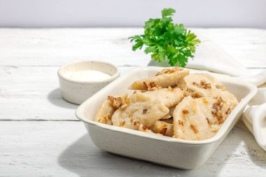 Lahanayla dolu börekler. Kızarmış soğan, taze ekşi krema. Geleneksel Ukrayna yemeği, moda vejetaryen yemekleri. Sert ışık, karanlık gölge, beyaz ahşap zemin, kopyalama alanı