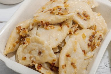 Lahanayla dolu börekler. Kızarmış soğan, taze ekşi krema. Geleneksel Ukrayna yemeği, moda vejetaryen yemekleri. Sert ışık, karanlık gölge, beyaz ahşap zemin, kapat