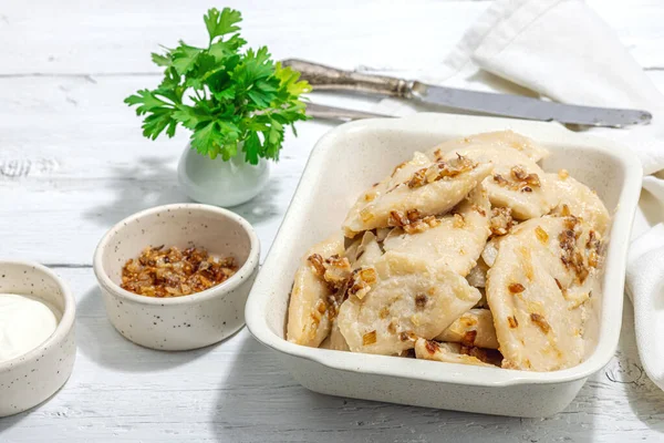 Lahanayla dolu börekler. Kızarmış soğan, taze ekşi krema. Geleneksel Ukrayna yemeği, moda vejetaryen yemekleri. Sert ışık, karanlık gölge, beyaz ahşap zemin, kapat