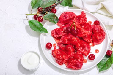 Hamur tatlısı, taze kiraz. Olgun meyveler, tatlı sos, taze ekşi krema. Geleneksel Ukrayna yemeği, moda vejetaryen yemekleri. Beyaz ahşap arka plan, sert ışık, koyu gölge, üst manzara