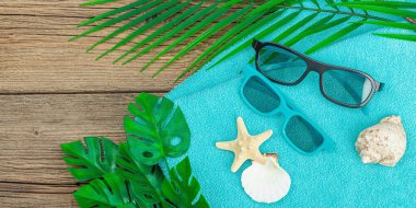 Yaz tatili kavramı. Banyo havlusu, güneş gözlüğü, deniz dekoru. Avuç içi ve canavar yaprakları, ahşap zemin, düz yatış, pankart biçimi