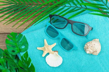 Yaz tatili kavramı. Banyo havlusu, güneş gözlüğü, deniz dekoru. Avuç içi ve canavar yaprakları, ahşap arka plan, düz yatak, yakın çekim