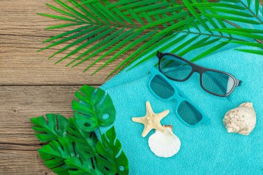 Yaz tatili kavramı. Banyo havlusu, güneş gözlüğü, deniz dekoru. Palmiye ve canavar yaprakları, ahşap zemin, düz yatış, kopyalama alanı
