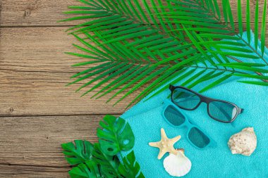 Yaz tatili kavramı. Banyo havlusu, güneş gözlüğü, deniz dekoru. Palmiye ve canavar yaprakları, ahşap zemin, düz yatış, üst manzara