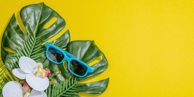 Yaz tatili kavramı. Güneş gözlüğü, deniz dekoru, palmiye ve canavar yaprakları, orkide çiçeği. Parlak sarı arkaplan, sert ışık, koyu gölge, düz uzanma, pankart biçimi