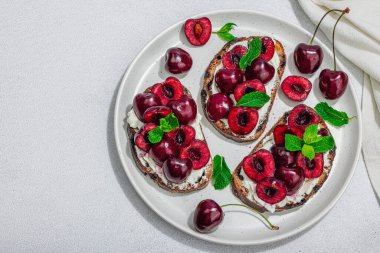 Tatlı kirazlı, krem peynirli ve nane yapraklı taze ekmek sandviçleri. Günaydın kahvaltı konsepti. Sert ışık, karanlık gölge, beyaz taş arka plan, üst görüş