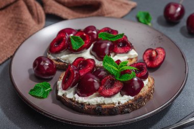 Tatlı kirazlı, krem peynirli ve nane yapraklı taze ekmek sandviçleri. Günaydın kahvaltı konsepti. Sert ışık, karanlık gölge, siyah taş beton arka plan, kapat