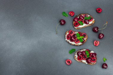 Tatlı kirazlı, krem peynirli ve nane yapraklı taze ekmek sandviçleri. Günaydın kahvaltı konsepti. Sert ışık, karanlık gölge, siyah taş arka plan, üst görüş