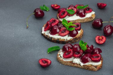Tatlı kirazlı, krem peynirli ve nane yapraklı taze ekmek sandviçleri. Günaydın kahvaltı konsepti. Sert ışık, karanlık gölge, siyah taş zemin, kopyalama alanı