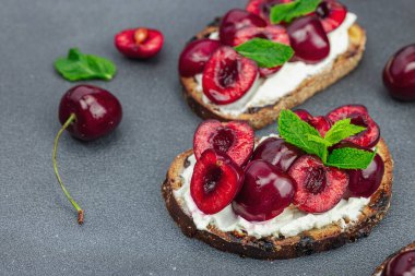 Tatlı kirazlı, krem peynirli ve nane yapraklı taze ekmek sandviçleri. Günaydın kahvaltı konsepti. Sert ışık, karanlık gölge, siyah taş zemin, kopyalama alanı