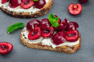 Tatlı kirazlı, krem peynirli ve nane yapraklı taze ekmek sandviçleri. Günaydın kahvaltı konsepti. Sert ışık, karanlık gölge, siyah taş beton arka plan, kapat