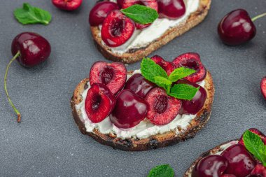 Tatlı kirazlı, krem peynirli ve nane yapraklı taze ekmek sandviçleri. Günaydın kahvaltı konsepti. Sert ışık, karanlık gölge, siyah taş beton arka plan, kapat