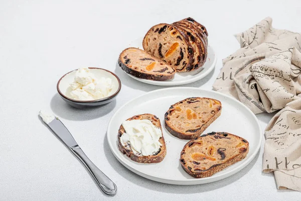 stock image Sweet bread with raisins, dried apricots, dates and figs. Healthy ingredient for sandwiches, breakfast concept. Hard light, dark shadow, white stone concrete background, copy space