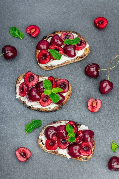 Stock image Fresh bread sandwiches with sweet cherry, cream cheese and mint leaves. Good morning breakfast concept. Hard light, dark shadow, black stone concrete background, top view