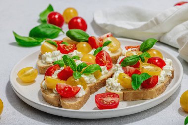 Domates kirazlı, krem peynirli ve fesleğenli taze ekmek sandviçleri. Sabah kahvaltısı kavramı. Sert ışık, karanlık gölge, beyaz taş beton arka plan, kapat
