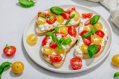 Domates kirazlı, krem peynirli ve fesleğenli taze ekmek sandviçleri. Sabah kahvaltısı kavramı. Sert ışık, karanlık gölge, beyaz taş beton arka plan, kapat