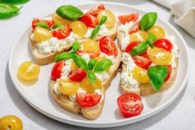 Domates kirazlı, krem peynirli ve fesleğenli taze ekmek sandviçleri. Sabah kahvaltısı kavramı. Sert ışık, karanlık gölge, beyaz taş beton arka plan, kapat